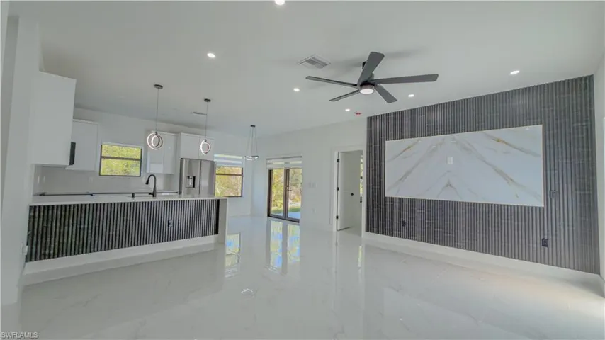 Unfurnished living room with an accent wall, recessed lighting, light marble finish floors, wallpapered walls, and french doors