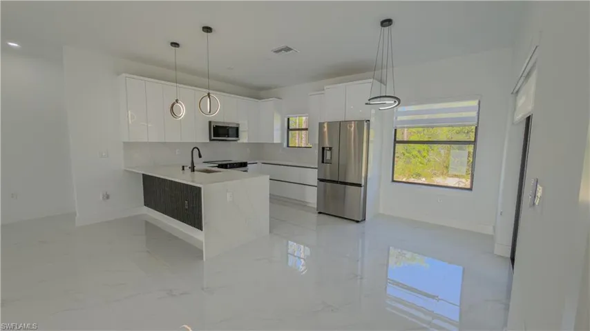 Kitchen with stainless steel appliances, white cabinets, light marble finish floors, pendant lighting, and a peninsula