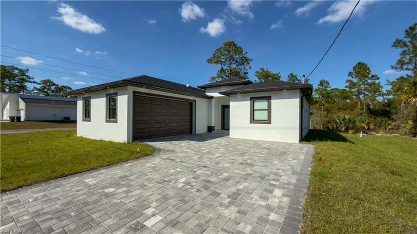 Prairie-style home featuring a front lawn, decorative driveway, stucco siding, and a garage
