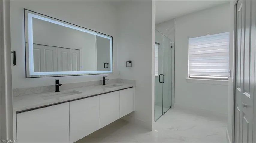 Full bath featuring double vanity, a marble finish shower, light marble finish floors, and a closet
