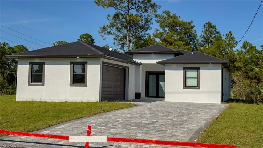 Prairie-style house featuring a front lawn, stucco siding, decorative driveway, and a garage