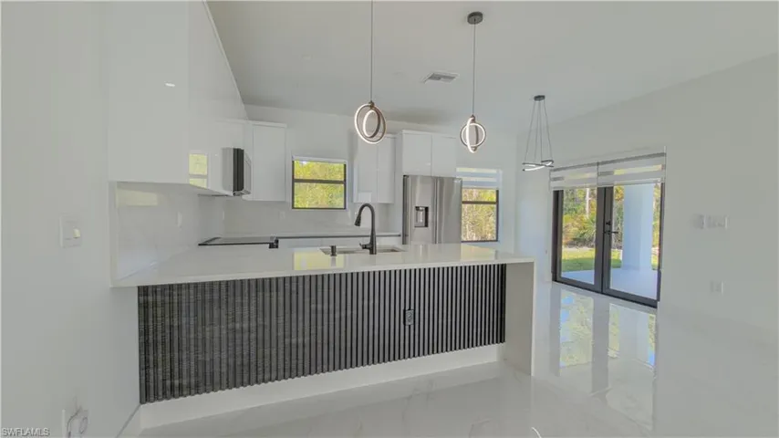 Kitchen featuring white cabinetry, light stone countertops, light marble finish flooring, pendant lighting, and stainless steel fridge with ice dispenser