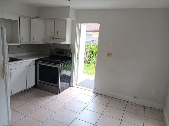 Kitchen with white cabinets, stainless steel electric range, light tile patterned floors, and freestanding refrigerator