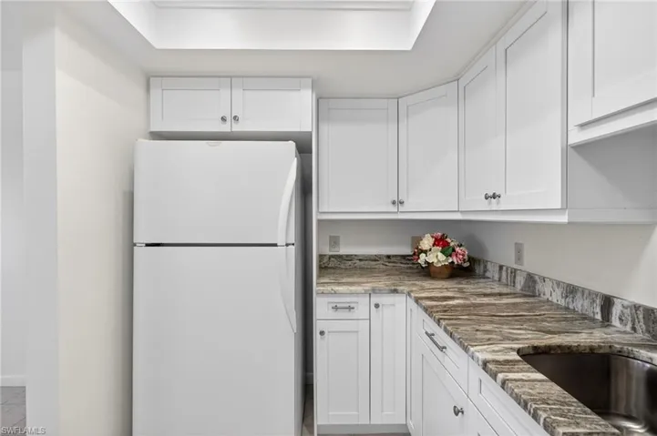 Kitchen featuring freestanding refrigerator, white cabinetry, and light stone counters