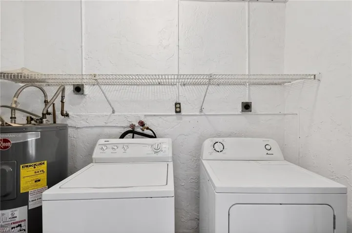 Laundry area with electric water heater, a textured wall, and washing machine and dryer