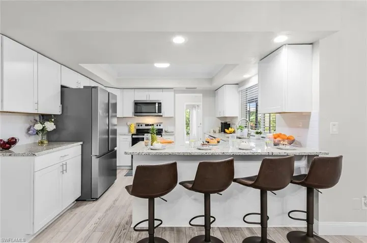 Modern kitchen with white cabinetry, stainless steel appliances, light-toned wood-finish flooring, recessed lighting, and an island with a light-toned countertop