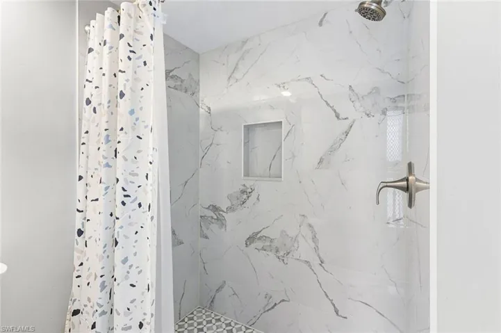 Shower featuring large format tile walls, mosaic tile flooring, built-in niche, and a brushed nickel showerhead and fixture