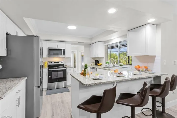 Bright kitchen featuring white shaker cabinetry, stainless steel appliances, a multi-level island with a light-toned countertop, and wood-finish flooring