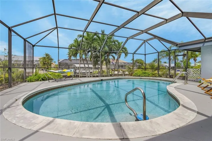 Screened-in pool deck featuring a free-form pool, stainless steel pool handrails, and a surrounding concrete patio