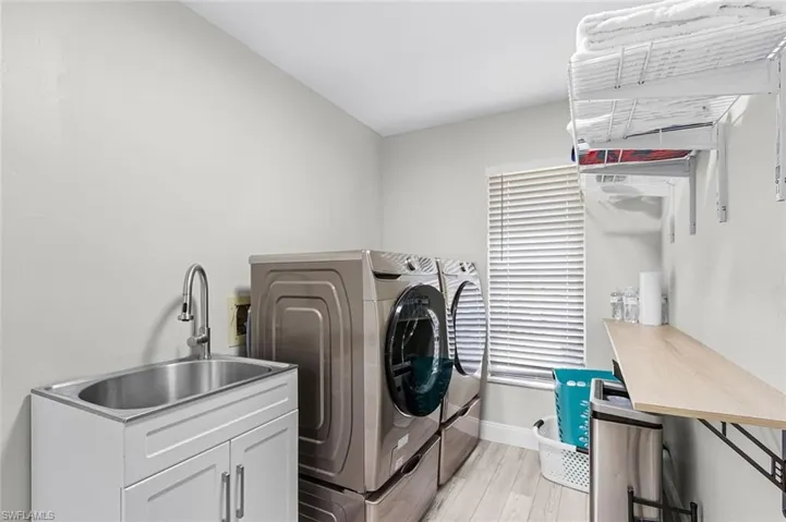 Laundry area with stacked appliances, a utility sink with white cabinetry, wood-finish flooring, and a window with blinds