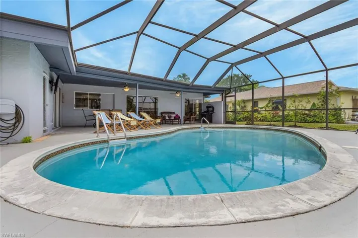 Screened enclosure featuring an oval-shaped pool with a textured concrete deck