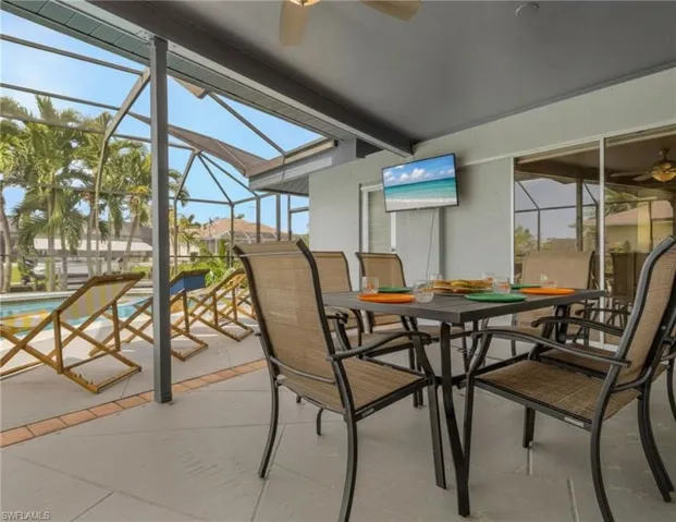 Screened-in lanai with a ceiling fan, mounted television, and outdoor dining area