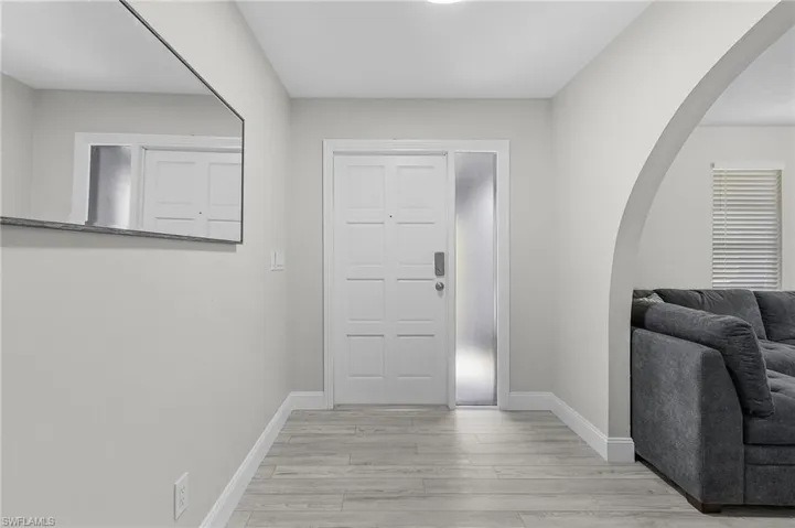 Entryway featuring wood-finish flooring, a paneled entry door with sidelight, and an arched doorway