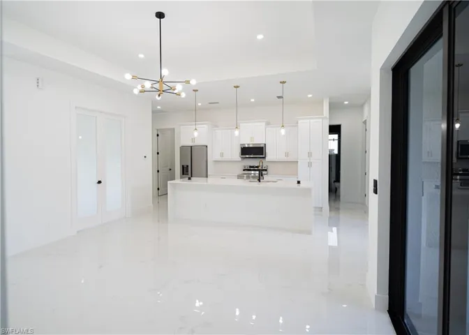 Kitchen featuring a kitchen island with sink, decorative light fixtures, appliances with stainless steel finishes, white cabinetry, and a chandelier