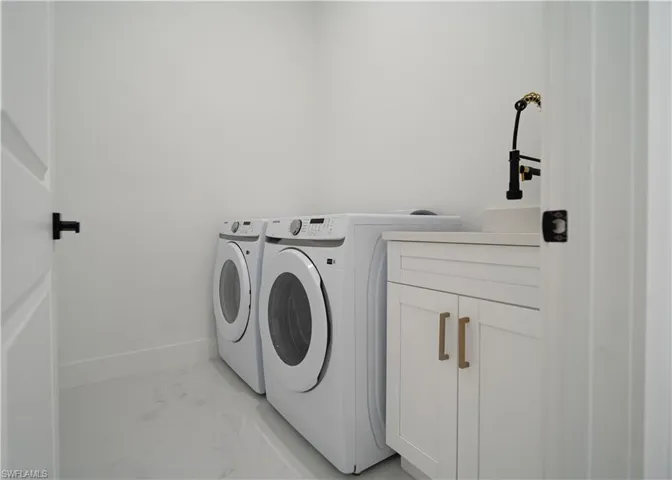 Laundry area featuring cabinet space, washer and clothes dryer, and light marble finish flooring