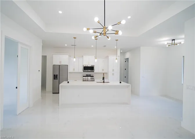 Kitchen with a chandelier, a tray ceiling, stainless steel appliances, an island with sink, and recessed lighting