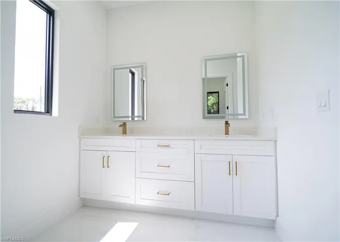 Bathroom with double vanity and light marble finish floors