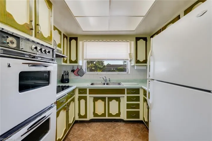 Kitchen featuring white appliances, green cabinetry, light countertops, and backsplash