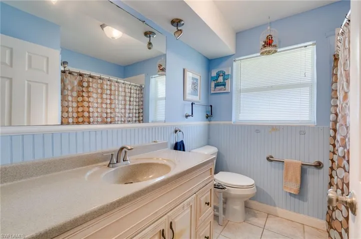 Bathroom with vanity, light tile patterned flooring, wainscoting, and a shower with curtain