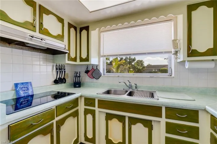 Kitchen featuring green cabinetry, light countertops, black electric stovetop, under cabinet range hood, and decorative backsplash