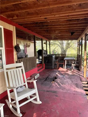 Covered exterior porch featuring exposed wood ceiling beams, painted flooring, and a wooden balustrade