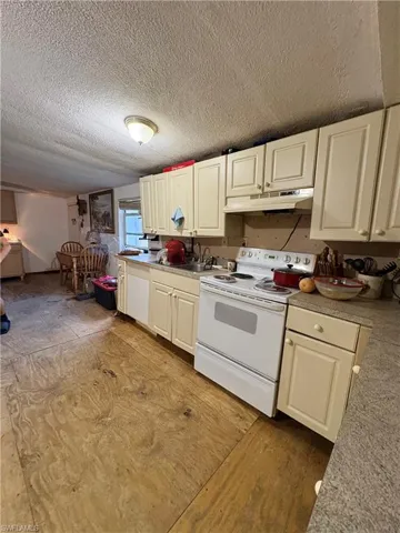 Kitchen featuring cabinetry with light-toned finish, speckled laminate countertops, white freestanding range, and a dual-basin stainless steel sink