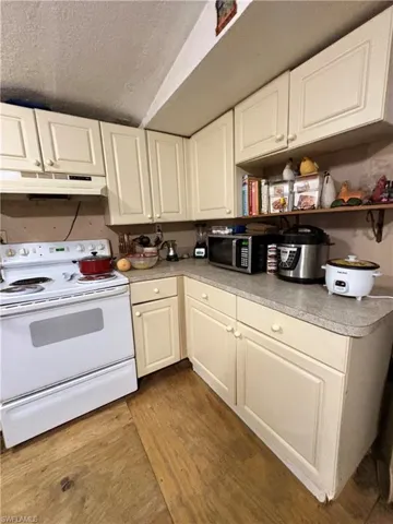 Kitchen featuring off-white cabinetry, solid-surface countertops, wood-finish flooring, and a white free-standing range with an integrated hood