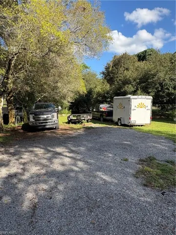 Gravel parking area bordered by mature trees and grass