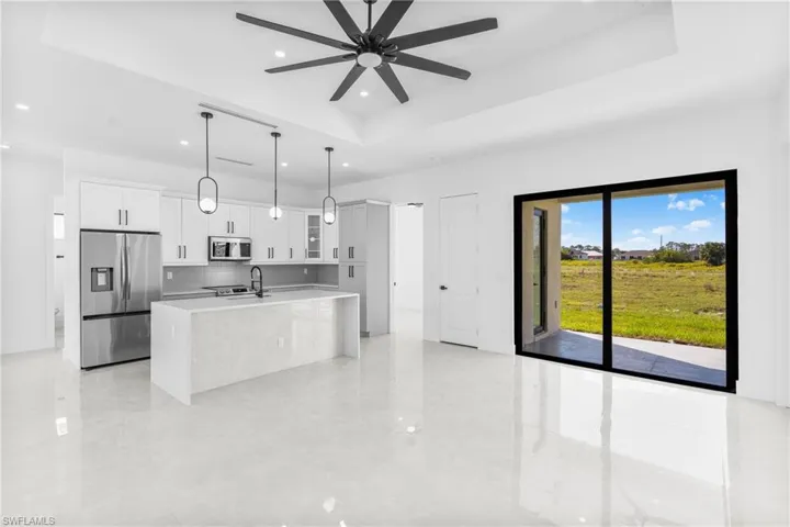 Kitchen with appliances with stainless steel finishes, a tray ceiling, glass insert cabinets, white cabinets, and an island with sink