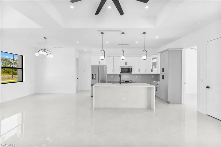 Kitchen with a raised ceiling, a center island with sink, decorative light fixtures, appliances with stainless steel finishes, and white cabinetry