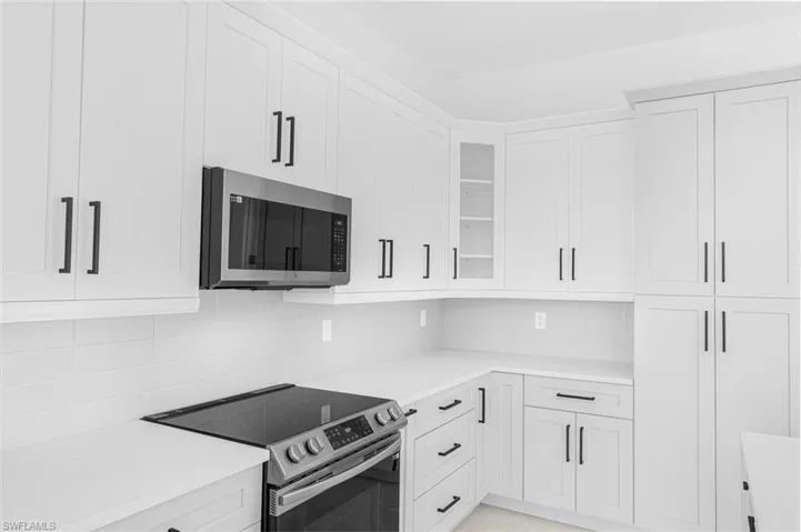 Kitchen with stainless steel appliances, tasteful backsplash, white cabinetry, and glass insert cabinets