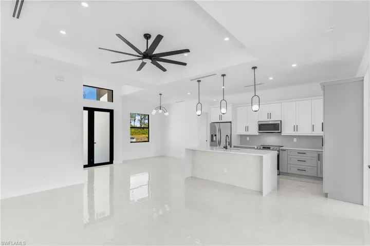 Kitchen with a tray ceiling, a center island with sink, white cabinetry, open floor plan, and hanging light fixtures