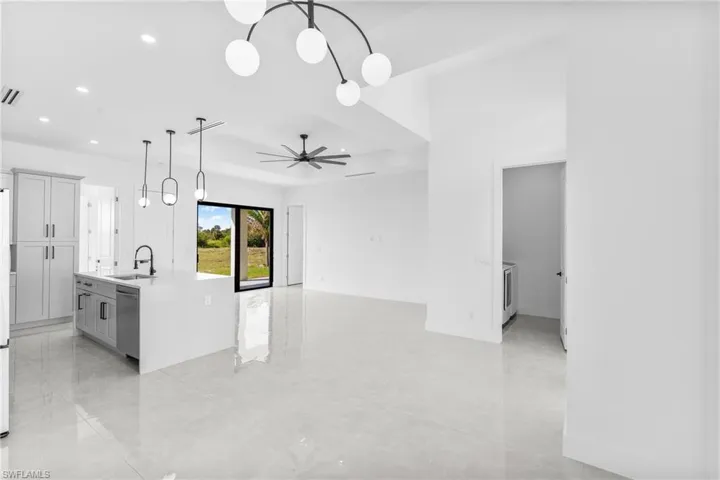 Kitchen with hanging light fixtures, a center island with sink, light stone counters, gray cabinets, and stainless steel dishwasher