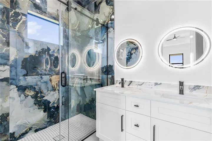 Full bath featuring double vanity, a marble finish shower, and ceiling fan