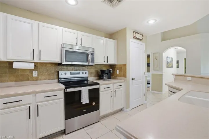 Kitchen featuring stainless steel appliances, light countertops, white cabinets, decorative backsplash, and arched walkways