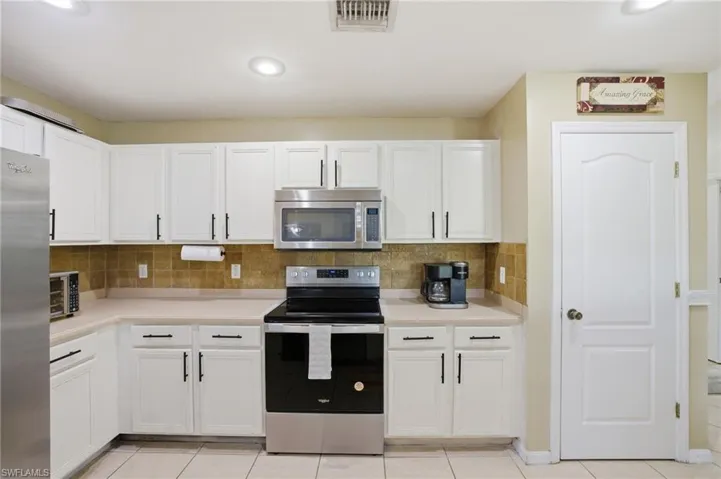 Kitchen featuring stainless steel appliances, white cabinetry, light countertops, and tasteful backsplash