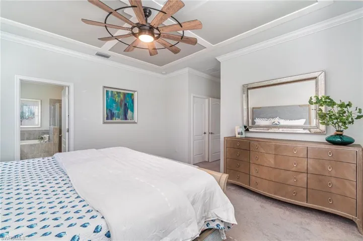 Bedroom with ornamental molding, light carpet, connected bathroom, and a ceiling fan