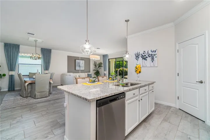 Kitchen with dishwasher, ornamental molding, hanging light fixtures, a kitchen island with sink, and white cabinetry