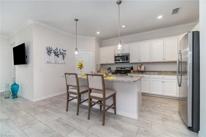 Kitchen with appliances with stainless steel finishes, ornamental molding, white cabinetry, light stone counters, and a kitchen breakfast bar