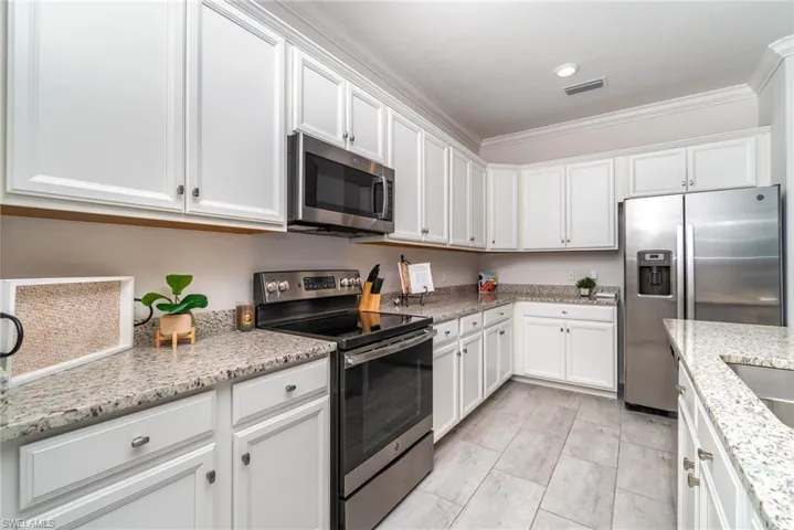 Kitchen featuring stainless steel appliances, white cabinets, crown molding, light stone counters, and recessed lighting