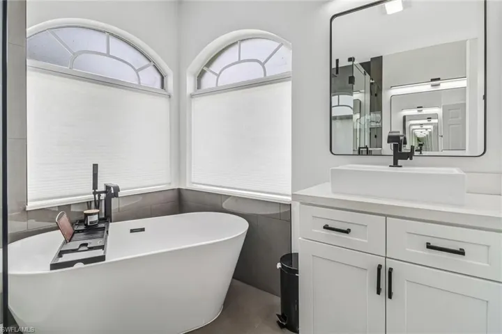 Bathroom with tile walls, tile patterned floors, a tub to relax in, and vanity