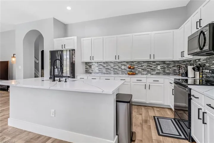 Kitchen featuring light hardwood / wood-style floors, appliances with stainless steel finishes, decorative backsplash, and an island with sink