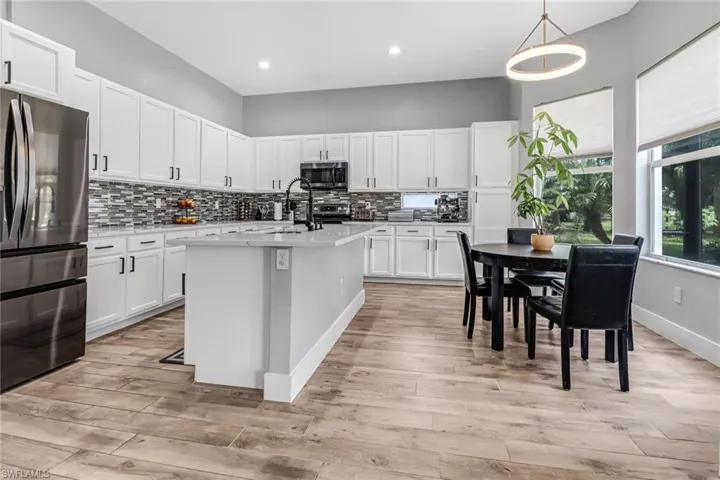 Kitchen featuring decorative backsplash, appliances with stainless steel finishes, light wood-type flooring, and a center island with sink