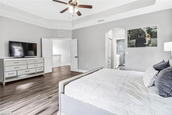 Bedroom with wood-type flooring, ceiling fan, and a tray ceiling