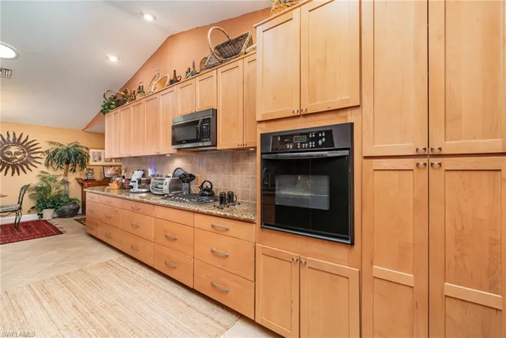 Kitchen with black appliances, backsplash, light tile flooring, vaulted ceiling, and light brown cabinets
