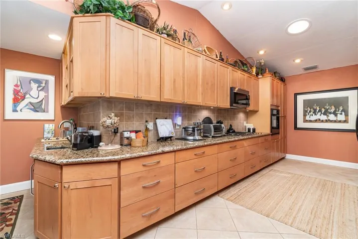Kitchen featuring backsplash, oven, light tile floors, and vaulted ceiling