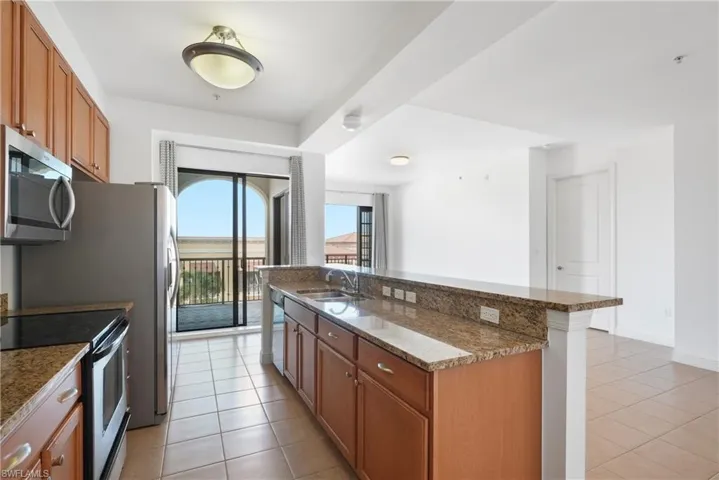 Kitchen featuring sink, appliances with stainless steel finishes, dark stone countertops, and light tile patterned floors