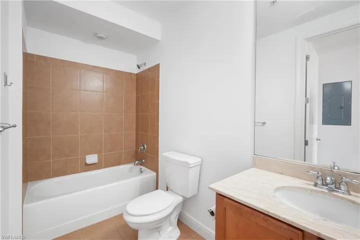 Full bathroom featuring toilet, vanity, tiled shower / bath combo, electric panel, and tile patterned flooring
