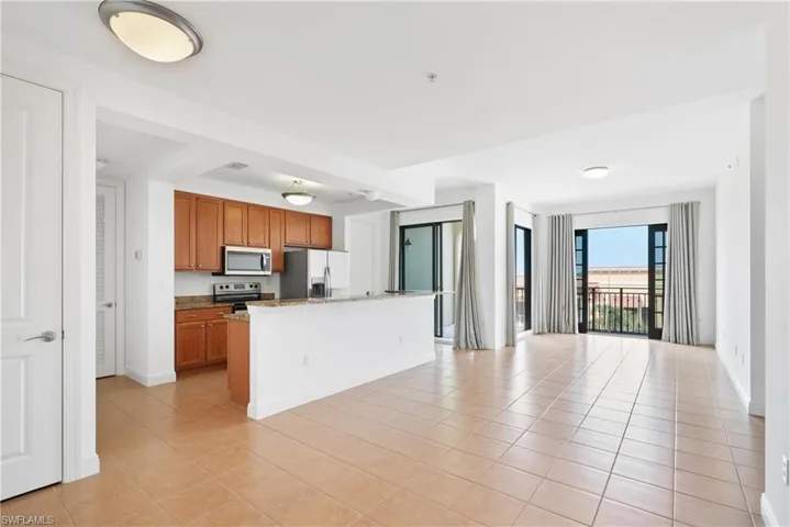 Kitchen with appliances with stainless steel finishes, light stone counters, a kitchen island with sink, and light tile patterned floors