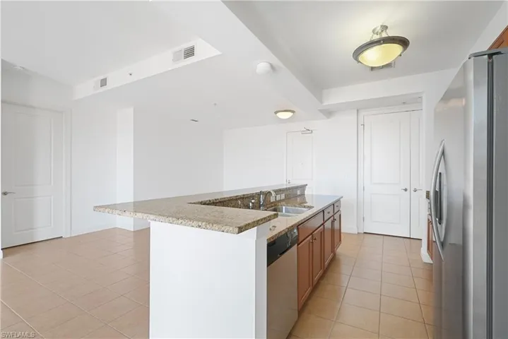 Kitchen featuring a kitchen island with sink, sink, light stone countertops, light tile patterned flooring, and appliances with stainless steel finishes